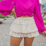 Frontal view of the One To Watch Skort In Cream that features an ivory faux-leather material, a thick elastic waist band with a tie detail, a tiered ruffle design, a shorts lining, and a flowy fit