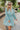 Frontal view of the Sincerely Yours Dress that features a light teal colored material, a collared V neckline, long cuffed sleeves, a smocked waist, a flowy fit, and a mini length.