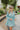 Frontal view of the Sincerely Yours Dress that features a light teal colored material, a collared V neckline, long cuffed sleeves, a smocked waist, a flowy fit, and a mini length.