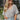 Front view of model wearing the Love Like This Bodysuit, which has an ivory and grey knit material with a floral print, a V surplice neckline, an oversized half sleeve, and a bikini bottom with a snap closure. Worn with denim shorts.