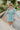 Frontal view of the Sincerely Yours Dress that features a light teal colored material, a collared V neckline, long cuffed sleeves, a smocked waist, a flowy fit, and a mini length.