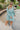 Frontal view of the Sincerely Yours Dress that features a light teal colored material, a collared V neckline, long cuffed sleeves, a smocked waist, a flowy fit, and a mini length.