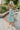 Side view of the Sincerely Yours Dress that features a light teal colored material, a collared V neckline, long cuffed sleeves, a smocked waist, a flowy fit, and a mini length.