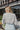 Back view of model wearing the Love Like This Bodysuit, which has an ivory and grey knit material with a floral print, a V surplice neckline, an oversized half sleeve, and a bikini bottom with a snap closure. Worn with denim shorts.