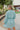 Back view of the Sincerely Yours Dress that features a light teal colored material, a collared V neckline, long cuffed sleeves, a smocked waist, a flowy fit, and a mini length.