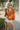Front view of model wearing the Forever Young Top in Caramel, which features a caramel colored silky material, a round neckline with a ruffle detail, a notched neckline with adjustable ties, long sleeves, and a flowy fit.