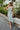 
Frontal view of the Endless Nights Midi Dress that features a white silk material, a sage green swirl print, a cowl neckline, a sleeveless design with thin adjustable straps, a side slit, and a midi length.
