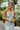 Frontal view of the Endless Nights Midi Dress that features a white silk material, a sage green swirl print, a cowl neckline, a sleeveless design with thin adjustable straps, a side slit, and a midi length.