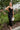 Frontal view of the Call You Mine Midi Dress that features a black colored silk material, a cowl neckline, a sleeveless design with thin adjustable straps, a side slit, and a midi length.