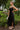 Side view of the Call You Mine Midi Dress that features a black colored silk material, a cowl neckline, a sleeveless design with thin adjustable straps, a side slit, and a midi length.