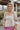 Frontal view of the Mystic Memory Top that features a taupe colored material, a straight neckline, a 3/4 sleeve, an open back with a tie closure, and a flowy fit.
