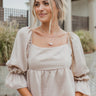 Frontal view of the Mystic Memory Top that features a taupe colored material, a straight neckline, a 3/4 sleeve, an open back with a tie closure, and a flowy fit.