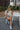Full body view of model wearing the Coast To Coast Sweater, which features a cream knit material with diamond stitching, a scoop neck, an oversized 3/4 sleeve, a thick bottom hem, and an oversized fit. Model shown sitting.