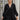 Frontal view of the Line Of Sight Dress In Black that features a black colored material, a round notched neckline with adjustable ties, long sleeves, vertical ruffle details, and a flowy fit.