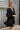 Side view of the Line Of Sight Dress In Black that features a black colored material, a round notched neckline with adjustable ties, long sleeves, vertical ruffle details, and a flowy fit.