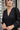Frontal view of the Line Of Sight Dress In Black that features a black colored material, a round notched neckline with adjustable ties, long sleeves, vertical ruffle details, and a flowy fit.