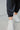 Close-up image of ankles - model is wearing the Trend Setter Pants, which feature a silky black material, a smocked waist, a ruffle detail at the hem, and a jogger fit. Worn with beige top.