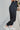 Close-up side view of model wearing the Trend Setter Pants, which feature a silky black material, a smocked waist, a ruffle detail at the hem, and a jogger fit.