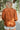 Back view of model wearing the Forever Young Top in Caramel, which features a caramel colored silky material, a round neckline with a ruffle detail, a notched neckline with adjustable ties, long sleeves, and a flowy fit.