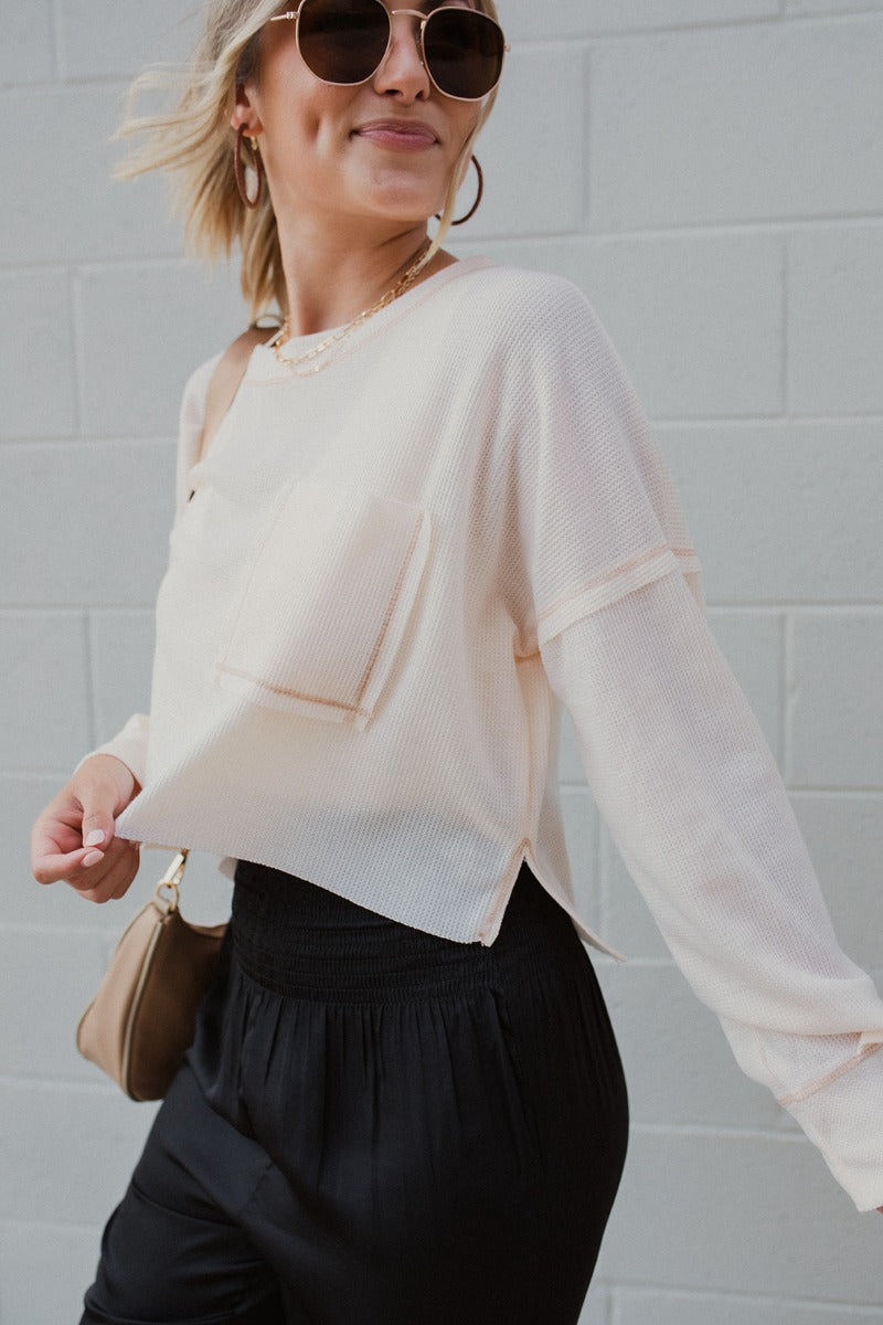 Frontal view of the Simple Life Top that features a cream thermal material, a scoop neck, a long sleeve, a front pocket, raw stitching, and a flowy fit.