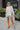 Frontal view of the Where To Next Top that features a soft cream material, a round neckline, a long cuffed sleeve, two side slits, and a thick bottom hem.