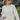 Frontal view of the Where To Next Top that features a soft cream material, a round neckline, a long cuffed sleeve, two side slits, and a thick bottom hem.