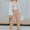 Full body front view of model wearing the Naomi Pants in Brown that have light brown lightweight fabric, two front pockets, a front zipper with a hook closure, and tapered legs