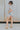 Full body side view of model wearing the Dreamy Floral Romper which features white, red, tan, sage, pink, muted yellow and blue cotton fabric, floral pattern, folded hem, two side pockets, two back pockets, button snap closure, two front chest pockets, co
