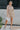 Full body front view of model wearing the Floral Haze Romper that has white denim fabric with a floral pattern, folded hems, pockets, snap closures, a collared neckline, and short sleeves