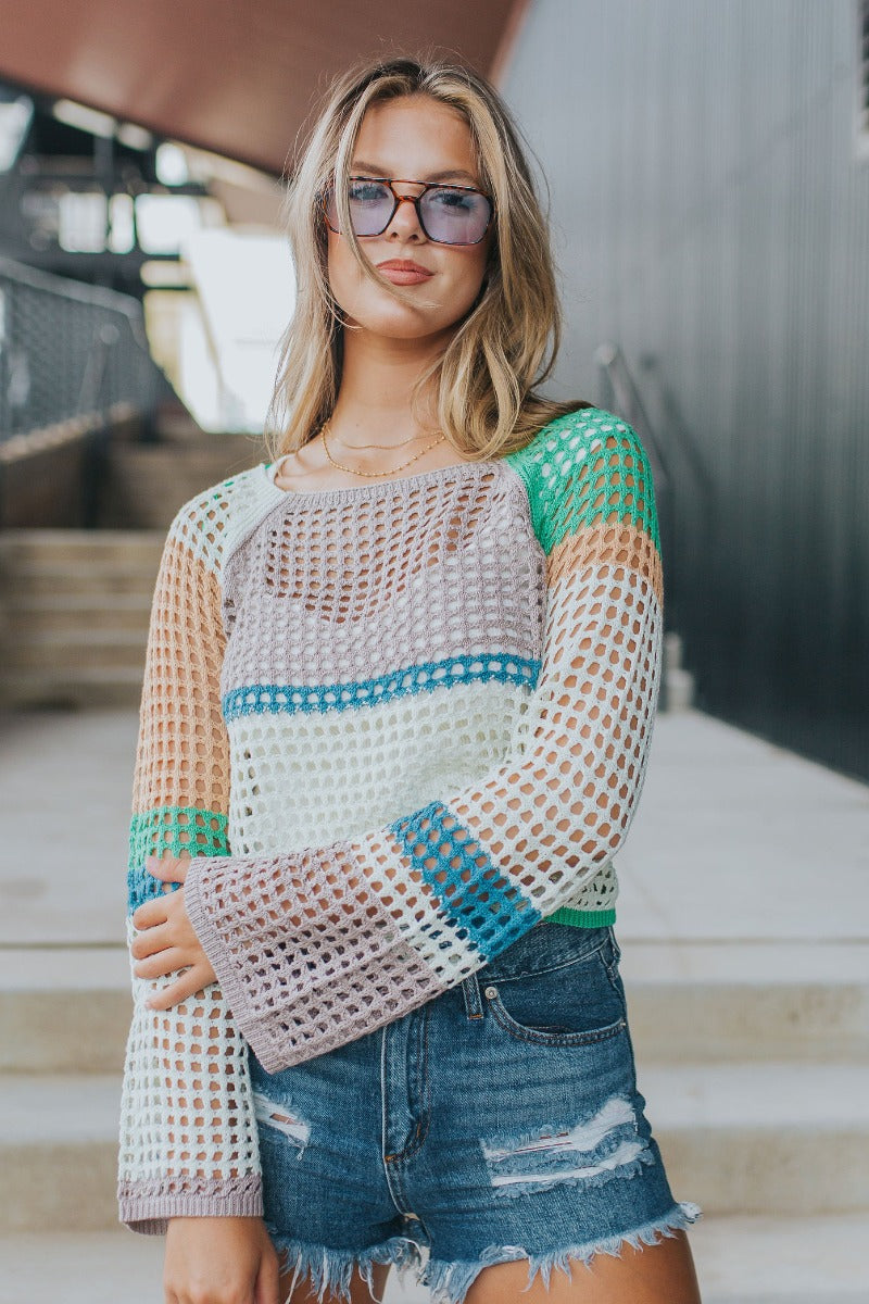 Front view of model wearing the Let It Be Sweater in Mint which features green, taupe, peach, blue and mint green open knit fabric, cropped waist, round neckline and long flare sleeves.