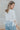 Back view of model wearing the Anywhere With You Top which features off white knit fabric, cropped waist, tassel hem details, open knit details, round neckline with monochrome stitch details and short sleeves with tassel hem details.