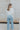 Full body back view of model wearing the Anywhere With You Top which features off white knit fabric, cropped waist, tassel hem details, open knit details, round neckline with monochrome stitch details and short sleeves with tassel hem details.