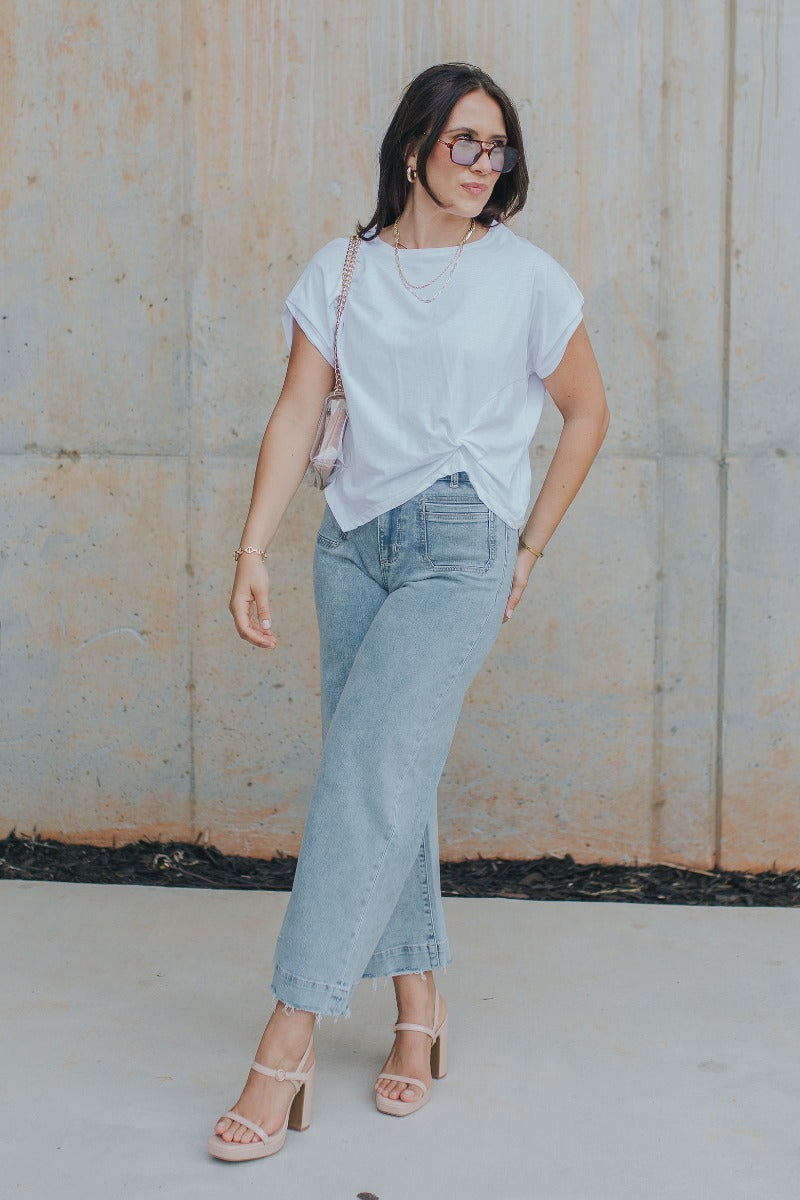 Full body view of model wearing the Tie The Knot Top which features white cotton fabric, side twist knot detail, round neckline and short sleeves.