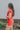 Side view of model wearing the Game On Romper which features washed red denim fabric, distressed details, two front pockets, one chest pocket, folded hem shorts, an elastic waistband in the back, a hidden zipper and button up closure, a collared neckline,