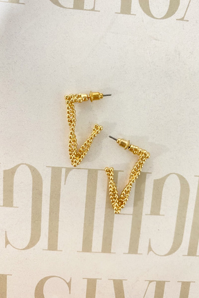 The Spaced Out Earring  is a gold dangle style earring, featuring a dotted, twist design with a V shape. 