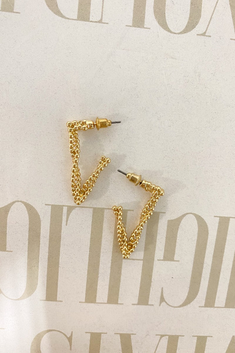 The Spaced Out Earring  is a gold dangle style earring, featuring a dotted, twist design with a V shape. 