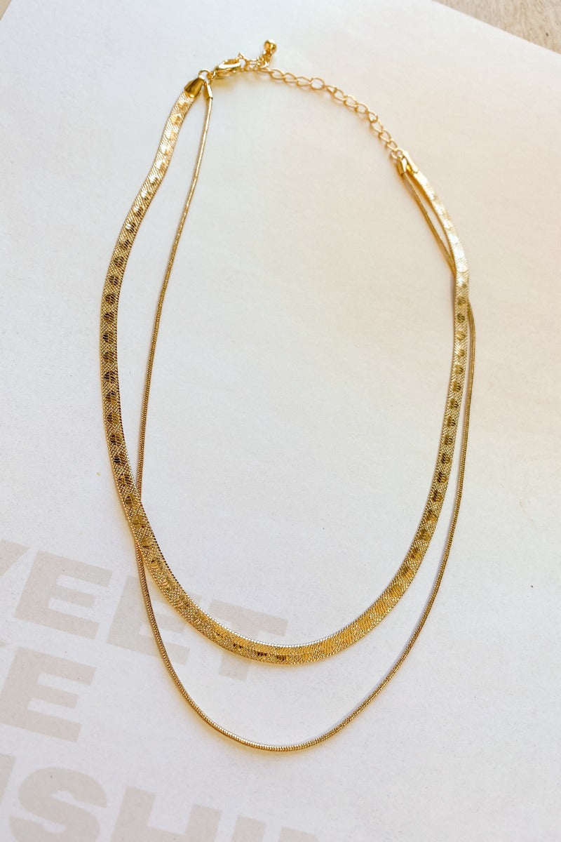 The Leave The Pieces Necklace is a gold, double layered necklace, featuring a herringbone chain and a thin snake chain finished with an adjustable link and clasp closure.