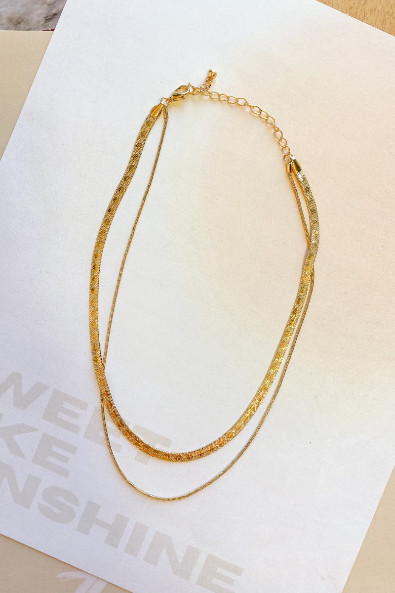 The Leave The Pieces Necklace is a gold, double layered necklace, featuring a herringbone chain and a thin snake chain finished with an adjustable link and clasp closure.