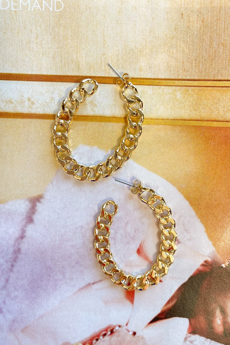 The One Earring is a gold hoop style earring, featuring an oval shape and a chain link design.