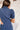 Back view of the Running The Show Denim Romper that features a navy colored denim with some stretch, a surplice neckline that snaps with a collar, half-length sleeves, a front zipper, pockets, pleating on the legs, and a 3" inseam.