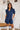 Frontal view of the Running The Show Denim Romper that features a navy colored denim with some stretch, a surplice neckline that snaps with a collar, half-length sleeves, a front zipper, pockets, pleating on the legs, and a 3" inseam.