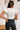 Back view of the Game-On Bodysuit that features a white ribbed material, a V neckline, a ruffled short sleeve, and a thong bottom with a snap closure.