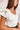 Frontal view of the Game-On Bodysuit that features a white ribbed material, a V neckline, a ruffled short sleeve, and a thong bottom with a snap closure.
