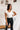 Frontal view of the Game-On Bodysuit that features a white ribbed material, a V neckline, a ruffled short sleeve, and a thong bottom with a snap closure.