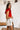 Side view of the Game-On Bodysuit that features a red ribbed material, a V neckline, a ruffled short sleeve, and a thong bottom with a snap closure.