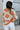 Back view of model wearing the Hello Sunshine Sweater, which features cream and orange knit fabric, orange ribbed trim, a large orange floral print, long sleeves, and an oversized fit