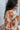 Side view of model wearing the Hello Sunshine Sweater, which features cream and orange knit fabric, orange ribbed trim, a large orange floral print, long sleeves, and an oversized fit