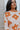Front view of model wearing the Hello Sunshine Sweater, which features cream and orange knit fabric, orange ribbed trim, a large orange floral print, long sleeves, and an oversized fit