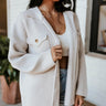 Front view of model wearing the Make You Mine Shacket, that has beige ribbed knit fabric, a button-up neckline with a collar and tortoise buttons, two front pockets, and long sleeves. Worn unbuttoned over white brami.