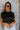 Front view of model wearing the Night Out Sequin Top, which features a sheer black sequin material, a round neck, short sleeves, a black liner, and a back zipper closure